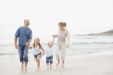 Smiling family holding hands and walking on beach. Photo : Momentimages