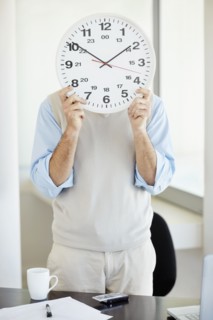 Office worker holding clock in front of face. Photo : Momentimages