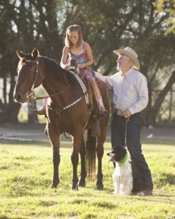 Senior man with dog assisting granddaughter (8-9) horseback riding in ranch. Photo : Mike Kemp