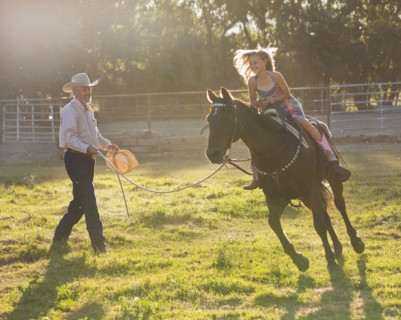 Trainer assisting girl (8-9) riding horse in paddock. Photo : Mike Kemp