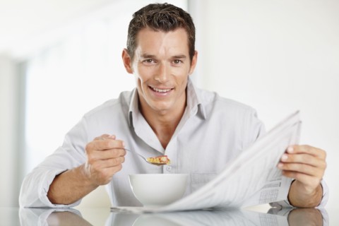 Cheerful mid adult man eating cornflakes and reading newspaper. Photo : Momentimages