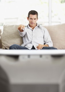 Mid adult man in front of televisionchanging channels. Photo : Momentimages