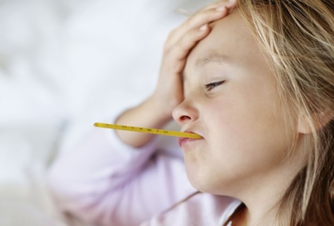 Sad girl (10-11) lying in bed with thermometer in mouth. Photo : Momentimages