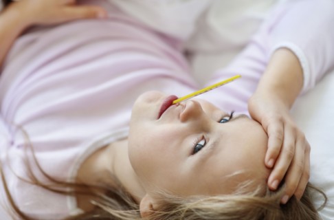 Sad girl (10-11) lying in bed with thermometer in mouth. Photo : Momentimages