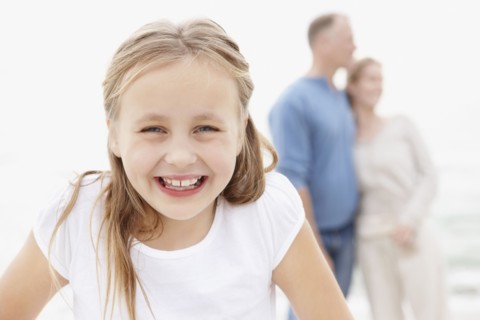 Portrait of smiling girl (10-11), embracing couple in the background. Photo : Momentimages