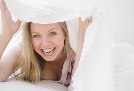 USA, New Jersey, Jersey City, Laughing attractive young woman emerging from under quilt. Photo :