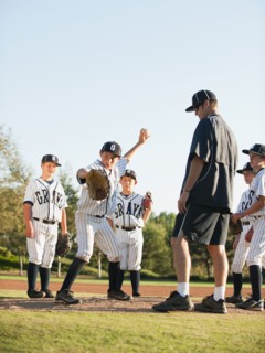 Baseball coach and boys (10-11) standing on baseball diamond.