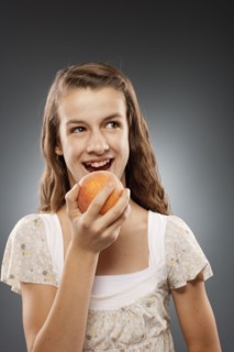 Girl (12-13) holding peach and laughing, studio shot. Photo : FBP
