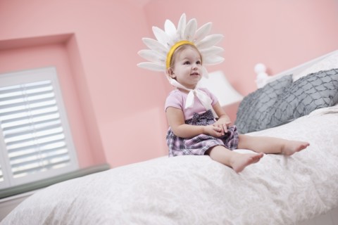USA, Utah, small girl (2-3) with plume sitting on bed. Photo : Tim Pannell