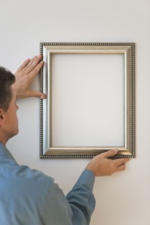 Man hanging silver frame on wall.