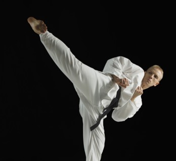 Young man performing karate kick on black background.