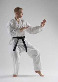 Young man performing karate stance on white background.