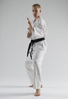 Young man performing karate stance on white background.