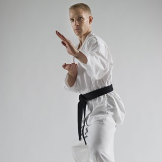 Young man performing karate stance on white background.