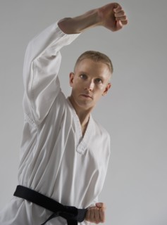 Young man performing karate stance on white background.