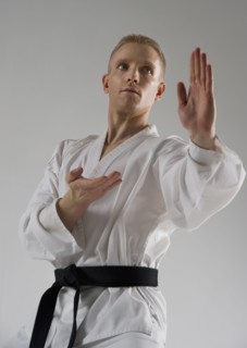 Young man performing karate stance on white background.
