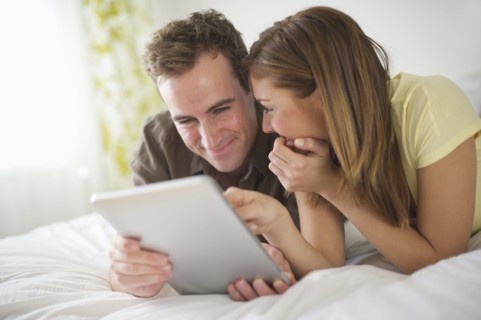 USA, New Jersey, Jersey City, Young couple with digital tablet lying on bed.