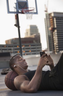 USA, Utah, Salt Lake City, Young man lying on basketball and listening to mp3 player. Photo : Mike