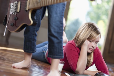 USA, Utah, Girl (10-11) reading magazine while another girl (6-7) playing guitar. Photo : Tim