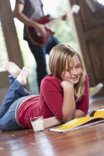 USA, Utah, Girl (10-11) reading magazine while man in the background playing guitar. Photo : Tim