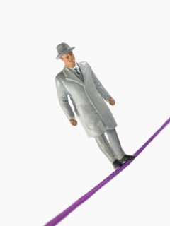 Studio shot of male figurine in suit balancing on tightrope. Photo : David Arky
