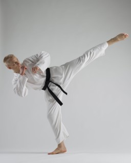 Young man performing karate kick on white background.