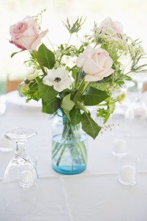 Vase of roses on set dinner table with glasses.
