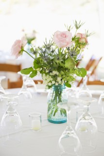 Vase of roses on set dinner table with glasses.