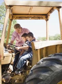 USA, New York, Flanders, Two boys (4-5, 8-9) with father sitting on tractor. Photo : Jamie Grill