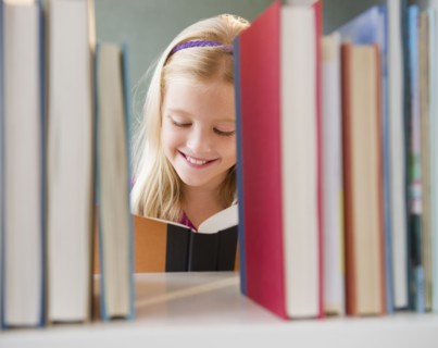 USA, New Jersey, Jersey City, View across the shelf showing girl (8-9) reading book. Photo : Jamie