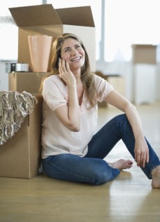 USA, New Jersey, Jersey City, Woman using mobile phone by boxes in new home.