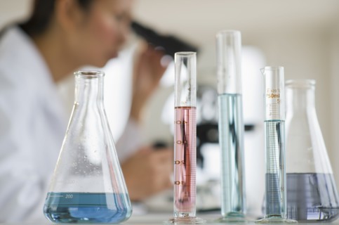 USA, New Jersey, Jersey City, Female scientist using microscope behind test tubes and flasks.