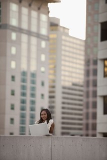 USA, Utah, Salt Lake City, Young businesswoman using laptop in front of skyscrapers. Photo : Mike
