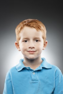 Portrait of smiling redhead boy (4-5) wearing blue polo shirt, studio shot. Photo : FBP