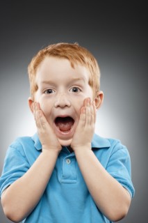 Portrait of smiling redhead boy (4-5) wearing blue polo shirt and looking surprised, studio shot.