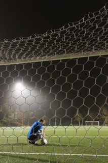 USA, California, Ladera Ranch, goalie on illuminated soccer field at night.