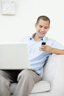 South Africa, Young man sitting on sofa with laptop and texting messages. Photo : momentimages