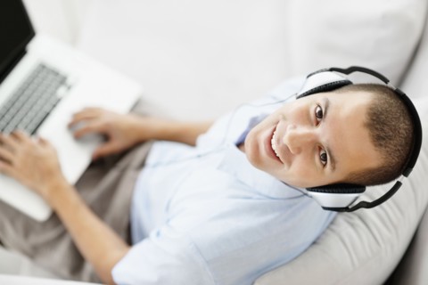 South Africa, Young man wearing headphones sitting on sofa and using laptop, high angle view. Photo