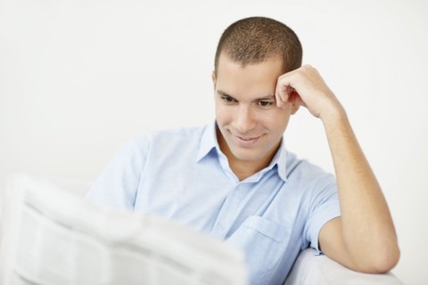 South Africa, Young smiling man reading newspaper. Photo : momentimages