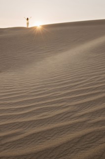 Woman with arms up, standing in desert.