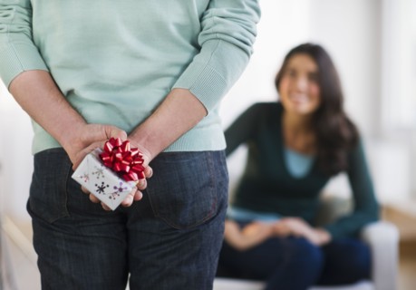 Young man with present behind his back, girlfriend in background. Photo : Daniel Grill
