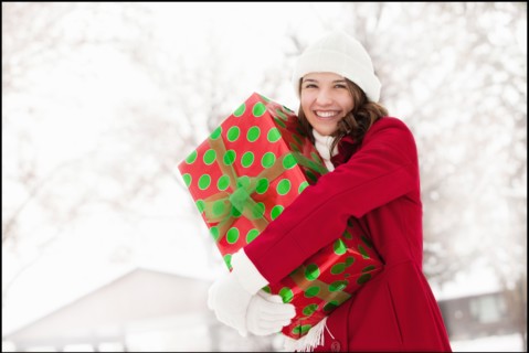 USA, Utah, Lehi, Portrait of young woman hugging Christmas gift outdoors. Photo : Mike Kemp
