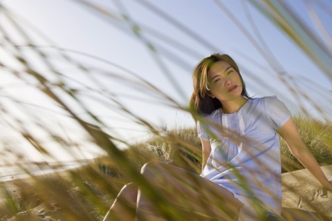 USA, California, Point Reyes, Young woman sitting in grass on sand dune. Photo : Noah Clayton