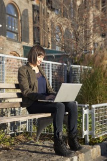 USA, New York City, Brooklyn, woman on bench using laptop. Photo : Shawn O'Connor