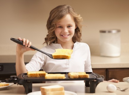 Portrait of girl (10-11) preparing toast in kitchen. Photo : Mike Kemp