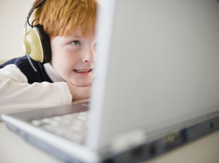 Boy (8-9) wearing headphones, using laptop. Photo : Jamie Grill Photography