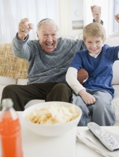 Grandfather and grandson (8-9) watching tv and cheering. Photo : Jamie Grill Photography