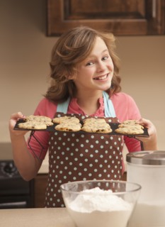 Portrait of girl (10-11) holding biscuits in kitchen. Photo : Mike Kemp