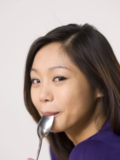 Young woman chewing spoon. Photo : Dan Bannister