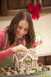 Young woman decorating gingerbread house in kitchen. Photo : Mike Kemp